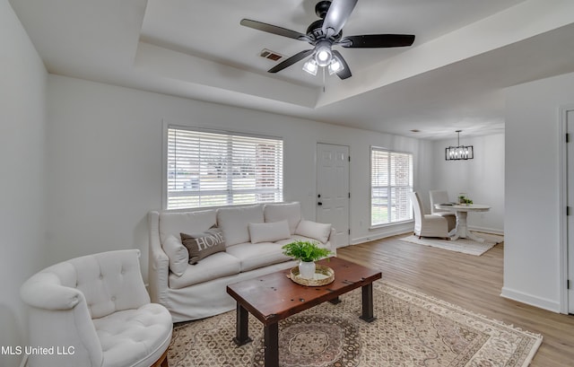 living room featuring visible vents, baseboards, a raised ceiling, light wood-style flooring, and ceiling fan with notable chandelier