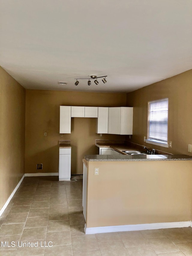 kitchen featuring white cabinets, kitchen peninsula, dark stone counters, and light tile patterned floors