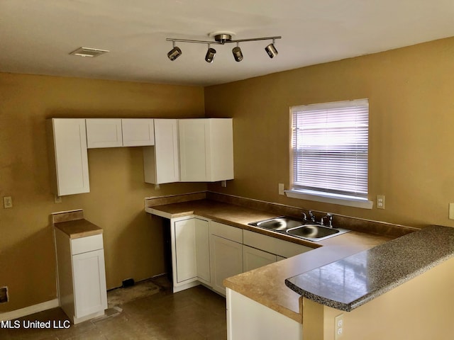 kitchen with dark tile patterned flooring, sink, kitchen peninsula, and white cabinets