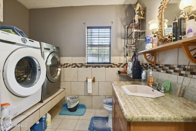 laundry room with sink, independent washer and dryer, a textured ceiling, light tile patterned floors, and tile walls