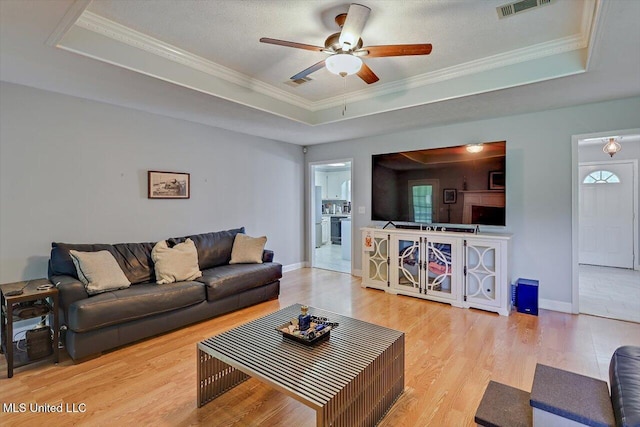 living area with a ceiling fan, a tray ceiling, wood finished floors, and visible vents