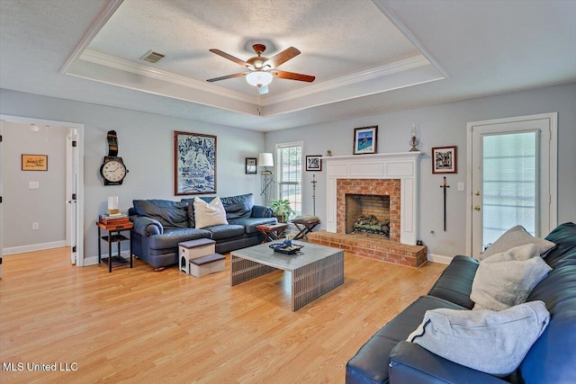 living area with ceiling fan, a tray ceiling, light wood-style flooring, and visible vents