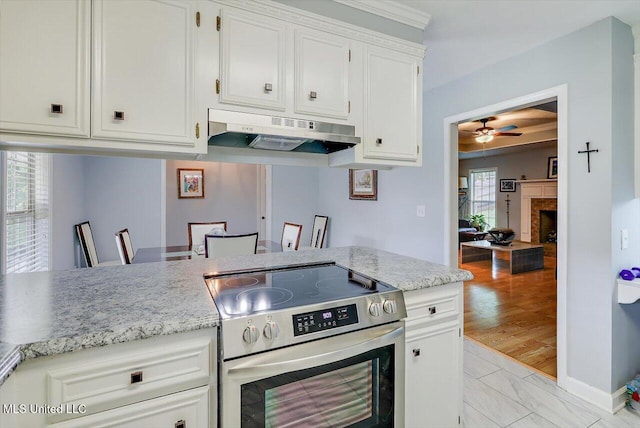 kitchen with a ceiling fan, a fireplace, under cabinet range hood, white cabinets, and electric stove