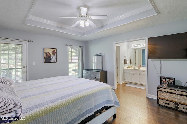 bedroom with ceiling fan, a raised ceiling, dark wood finished floors, ensuite bathroom, and ornamental molding