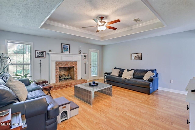 living area with visible vents, ornamental molding, light wood-style floors, a tray ceiling, and a ceiling fan
