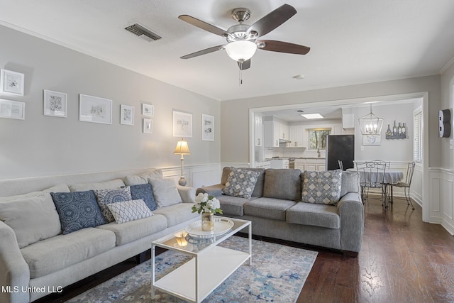 living area featuring visible vents, a wainscoted wall, dark wood-style flooring, and ceiling fan with notable chandelier