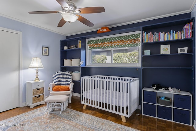 bedroom with baseboards, a crib, crown molding, and a ceiling fan