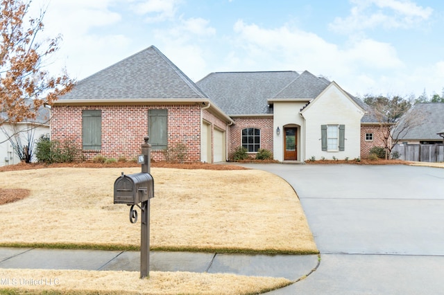 french provincial home with driveway, a shingled roof, an attached garage, fence, and brick siding