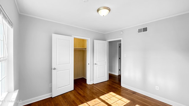 unfurnished bedroom featuring ornamental molding, dark wood-type flooring, multiple windows, and a closet