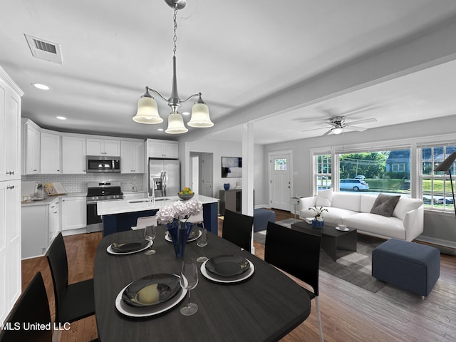 dining space featuring sink, hardwood / wood-style floors, ceiling fan with notable chandelier, and plenty of natural light