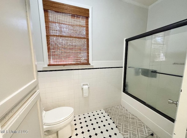 bathroom featuring tile patterned flooring, combined bath / shower with glass door, toilet, tile walls, and ornamental molding