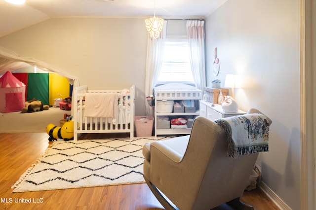 bedroom with lofted ceiling, wood-type flooring, and a nursery area