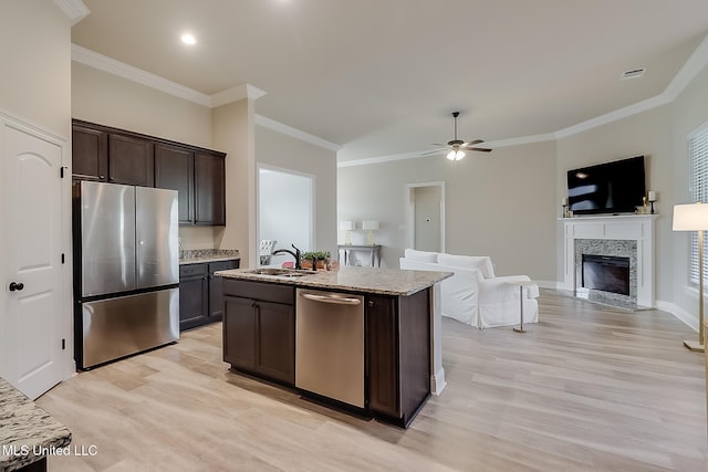 kitchen with dark brown cabinets, stainless steel appliances, a kitchen island with sink, sink, and a premium fireplace