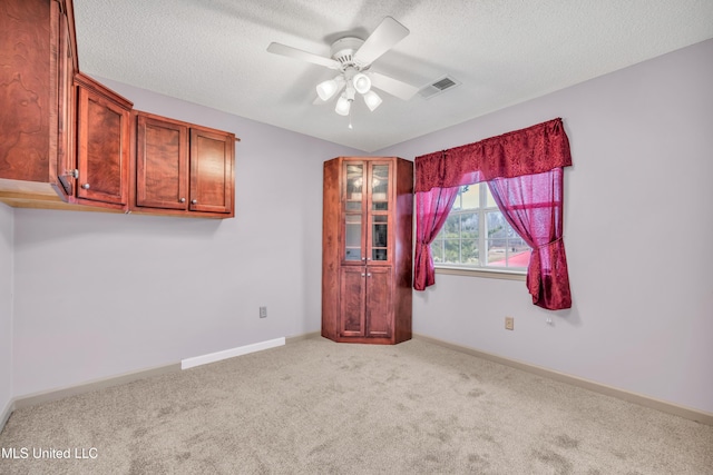 empty room with carpet floors, visible vents, ceiling fan, and a textured ceiling