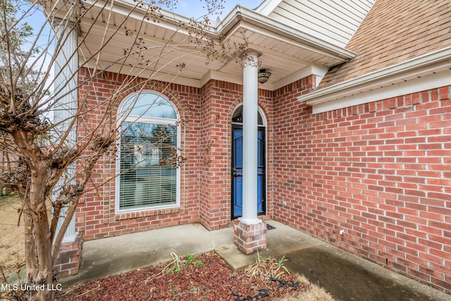 doorway to property featuring brick siding and roof with shingles