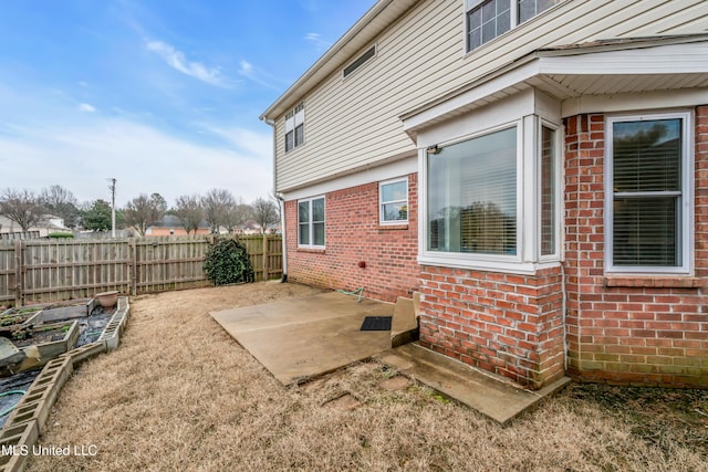 view of property exterior featuring a patio area, a fenced backyard, a vegetable garden, and brick siding