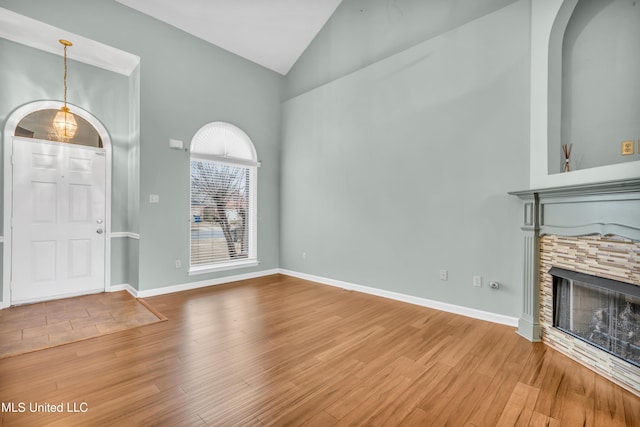 entrance foyer with a stone fireplace, wood-type flooring, and high vaulted ceiling