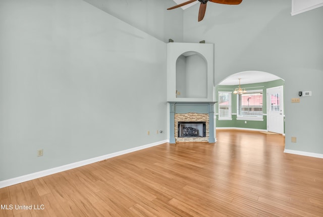 unfurnished living room with a towering ceiling, light wood-style flooring, baseboards, and ceiling fan with notable chandelier