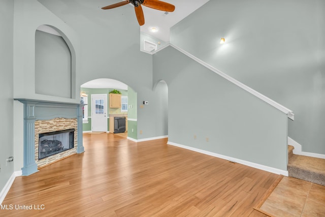 unfurnished living room featuring a fireplace, light wood finished floors, a towering ceiling, baseboards, and stairs