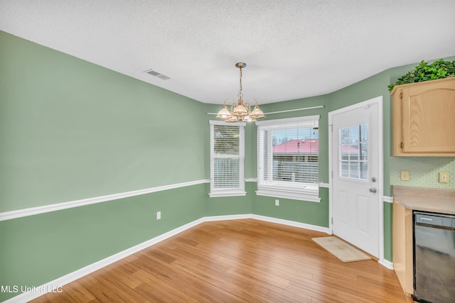 unfurnished dining area with visible vents, light wood-style flooring, baseboards, and an inviting chandelier