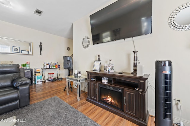 living area featuring a glass covered fireplace, visible vents, and light wood-style floors