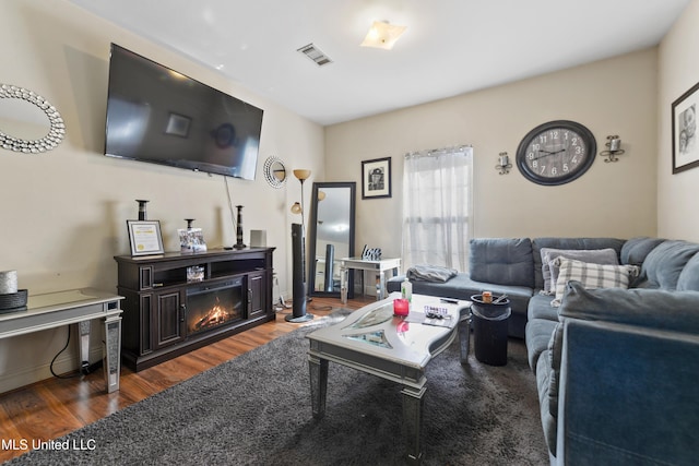 living area with a glass covered fireplace, visible vents, and wood finished floors