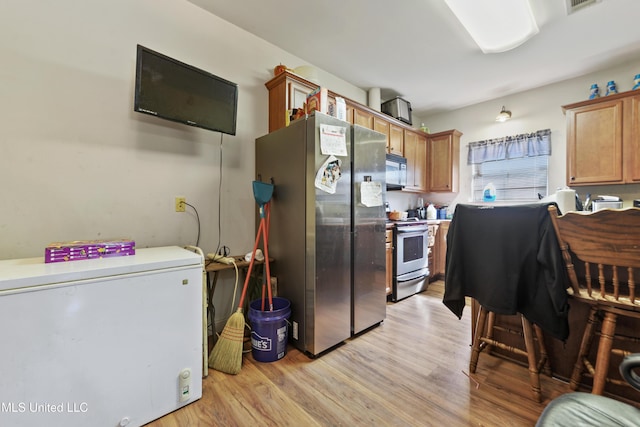 kitchen featuring stainless steel appliances, brown cabinetry, visible vents, and light wood-style floors