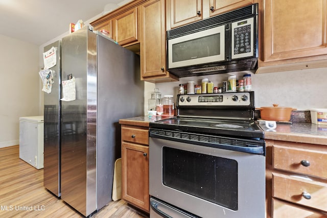 kitchen featuring baseboards, stainless steel appliances, brown cabinetry, and light wood-style floors