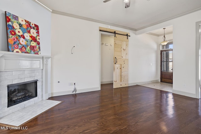 unfurnished living room with hardwood / wood-style flooring, ceiling fan, a fireplace, ornamental molding, and a barn door