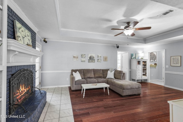 215 Cobblestone Dr, Madison, MS 39110 - living room featuring a tray ceiling, ornamental molding, a ceiling fan, a brick fireplace, and wood finished floors