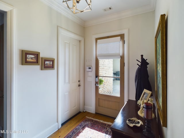 doorway to outside featuring light hardwood / wood-style floors, ornamental molding, and an inviting chandelier