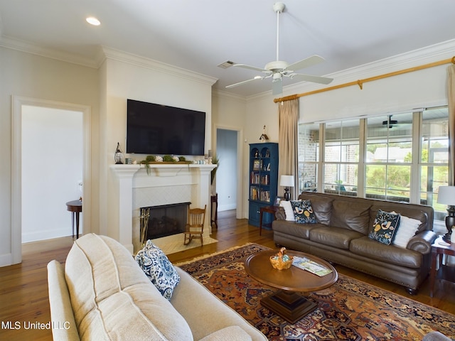 living room with a fireplace, crown molding, ceiling fan, and dark wood-type flooring