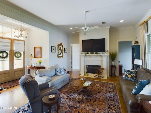 living room featuring wood-type flooring, ceiling fan with notable chandelier, plenty of natural light, and ornamental molding