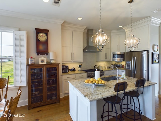 kitchen featuring pendant lighting, a kitchen island with sink, wall chimney range hood, sink, and stainless steel appliances