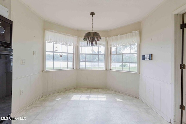 unfurnished dining area with a wainscoted wall, plenty of natural light, and a notable chandelier