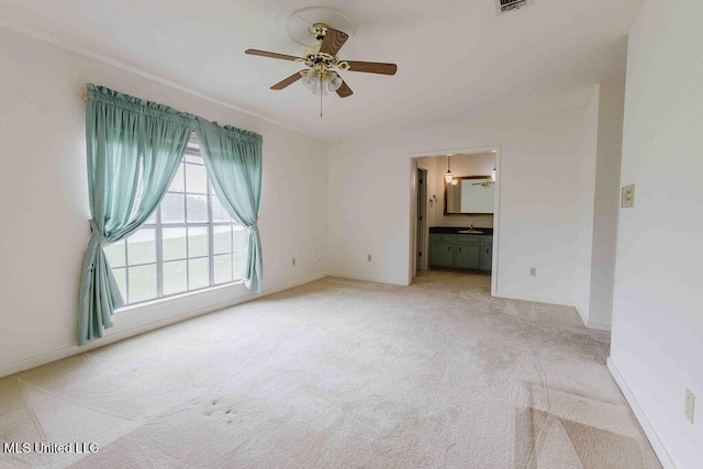 empty room featuring light colored carpet, a ceiling fan, baseboards, and a sink