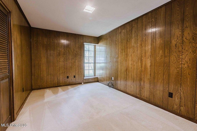 spare room featuring baseboards, wood walls, and light colored carpet