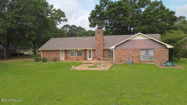 rear view of property featuring a chimney, a lawn, brick siding, cooling unit, and a patio