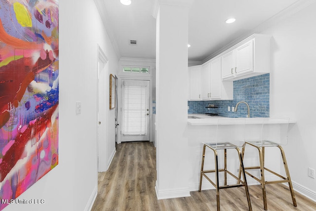 kitchen with decorative backsplash, a breakfast bar area, white cabinetry, light hardwood / wood-style flooring, and ornamental molding