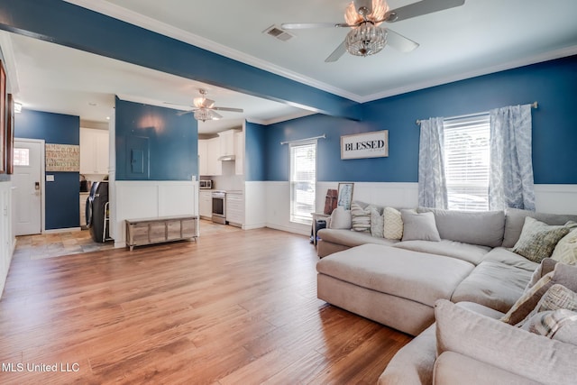 living area with visible vents, light wood-style flooring, wainscoting, and ceiling fan
