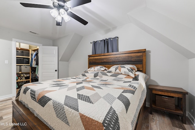 bedroom featuring a walk in closet, visible vents, vaulted ceiling, and wood finished floors