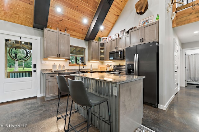 kitchen featuring a kitchen island, glass insert cabinets, appliances with stainless steel finishes, dark stone countertops, and a kitchen bar