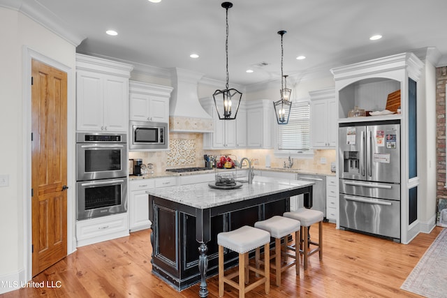 kitchen with light stone countertops, appliances with stainless steel finishes, light hardwood / wood-style floors, premium range hood, and a center island with sink