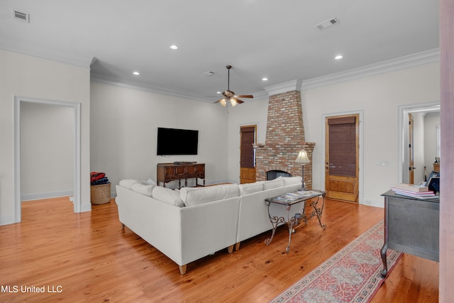 living room featuring ceiling fan, ornamental molding, light wood-type flooring, and a fireplace