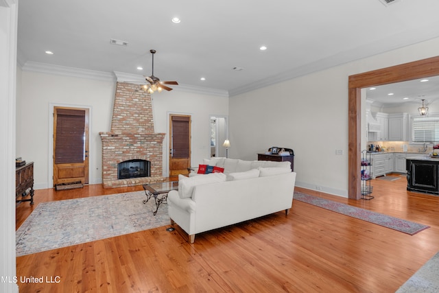 living room featuring ornamental molding, a brick fireplace, light hardwood / wood-style floors, and ceiling fan