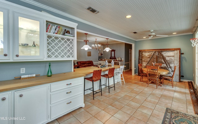 kitchen with built in desk, hanging light fixtures, crown molding, light tile patterned floors, and white cabinetry