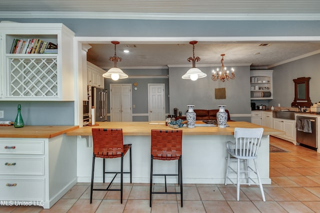 kitchen featuring pendant lighting, butcher block counters, stainless steel appliances, and a kitchen bar