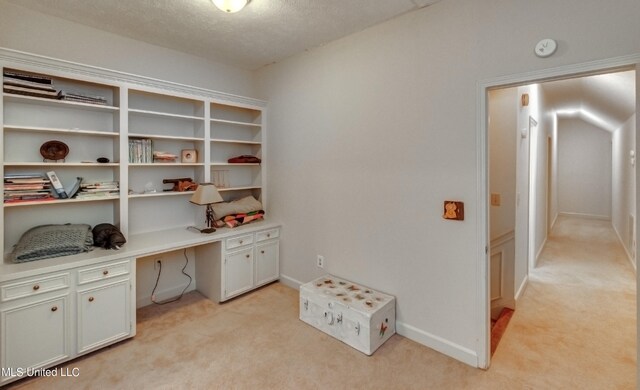 office space featuring a textured ceiling, light colored carpet, and built in desk