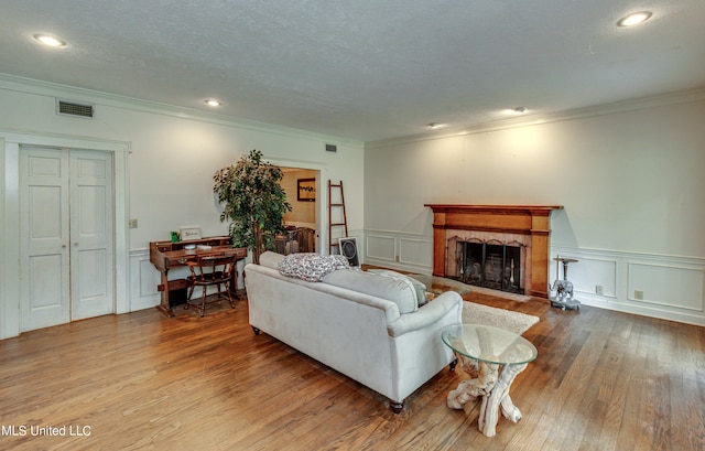 living room featuring a textured ceiling, wood-type flooring, ornamental molding, and a tile fireplace