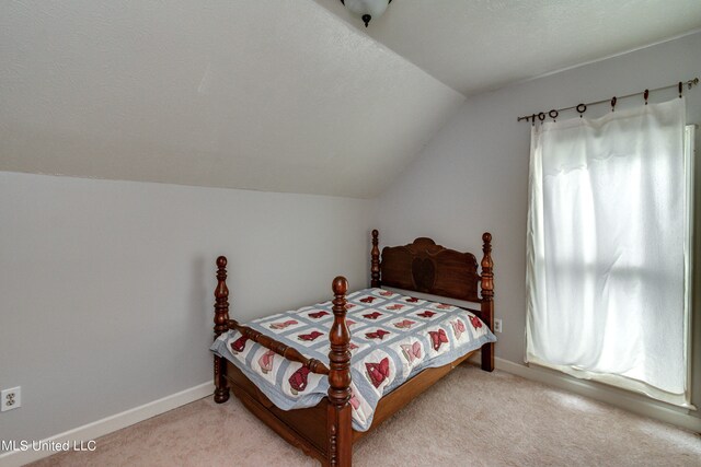 bedroom with a textured ceiling, light colored carpet, and vaulted ceiling